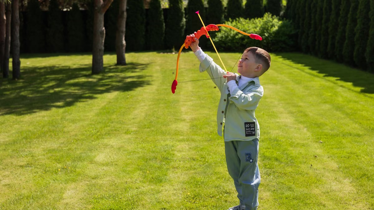 Young boy enjoying playtime with a toy bow and arrow in a lush green garden setting.